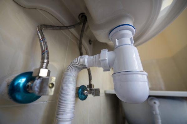 Bottom view of new white washbasin sink connected to sewer on background of bathroom light beige ceramic tiles. Professional plumbing and installation concept.